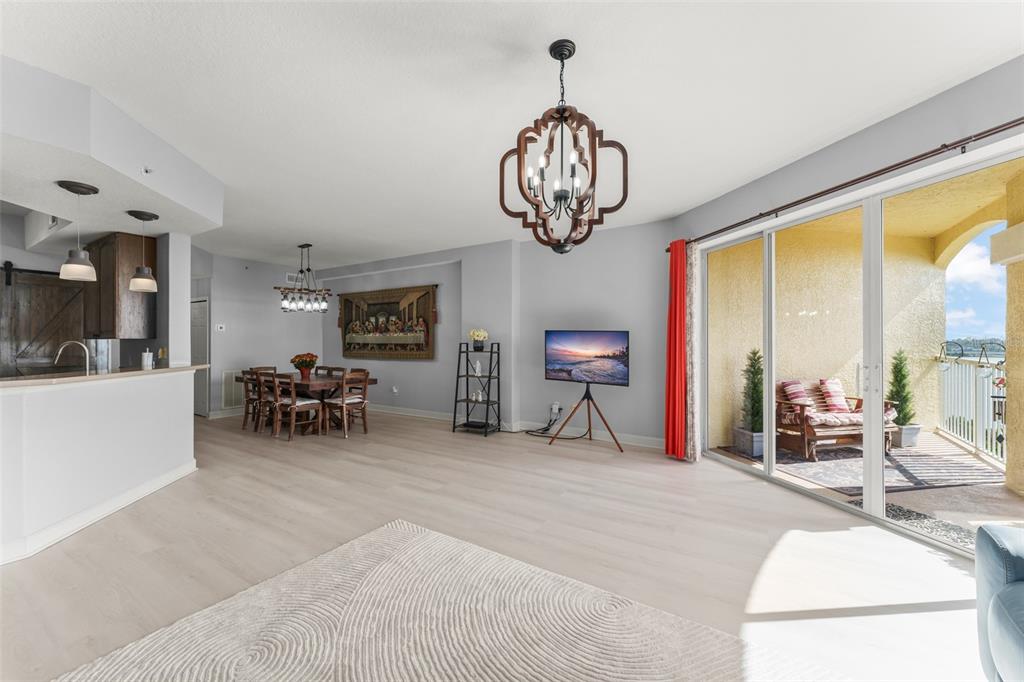 An open-concept living and dining area features light wood floors, a chandelier, and a balcony — 6336 BUFORD STREET UNIT 809, ORLANDO, FL