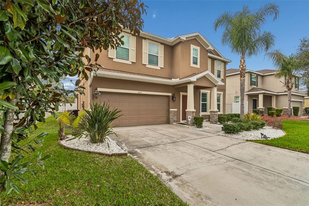A two-story tan house with a two-car garage, a concrete driveway, and a palm tree — 6105 MERRIFIELD DRIVE, ZEPHYRHILLS, FL