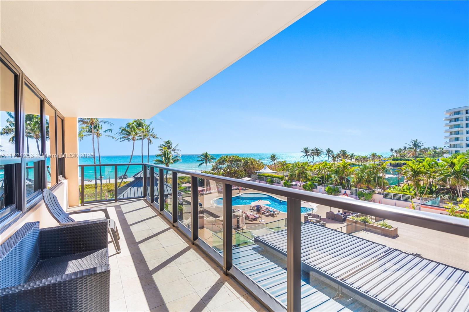 A balcony with outdoor furniture overlooks a swimming pool, palm trees, and the ocean — 5225 Collins Ave # 501, Miami Beach FL 33140, MIAMI BEACH, FL