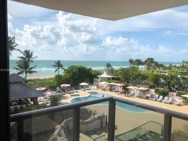 A balcony view overlooks a swimming pool, palm trees, and the ocean — 5225 Collins Ave # 501, Miami Beach FL 33140, MIAMI BEACH, FL