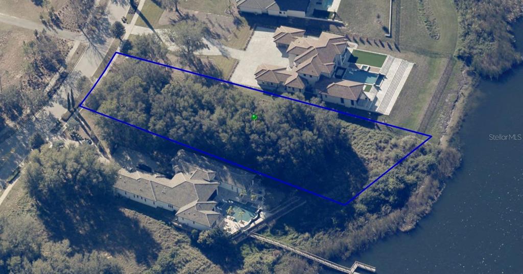 An aerial view shows two houses near a lake with a wooden dock and trees — 15345 PENDIO DRIVE, BELLA COLLINA, FL