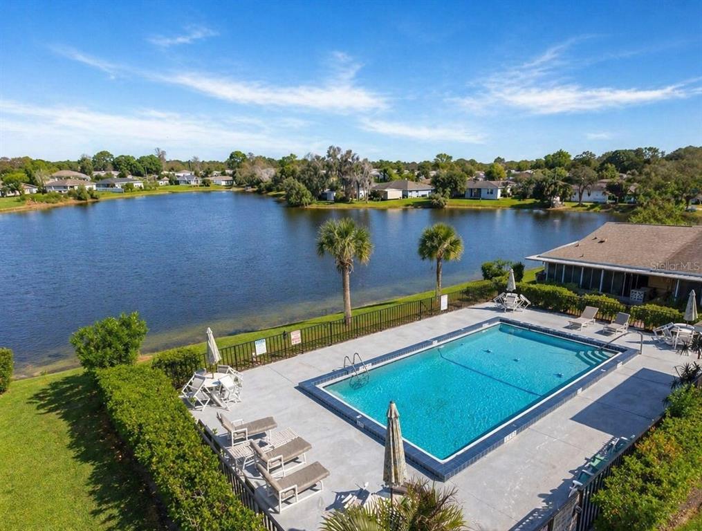 An aerial view shows a rectangular swimming pool with lounge chairs beside a large lake — 67 E COUNTRY COVE WAY, KISSIMMEE, FL