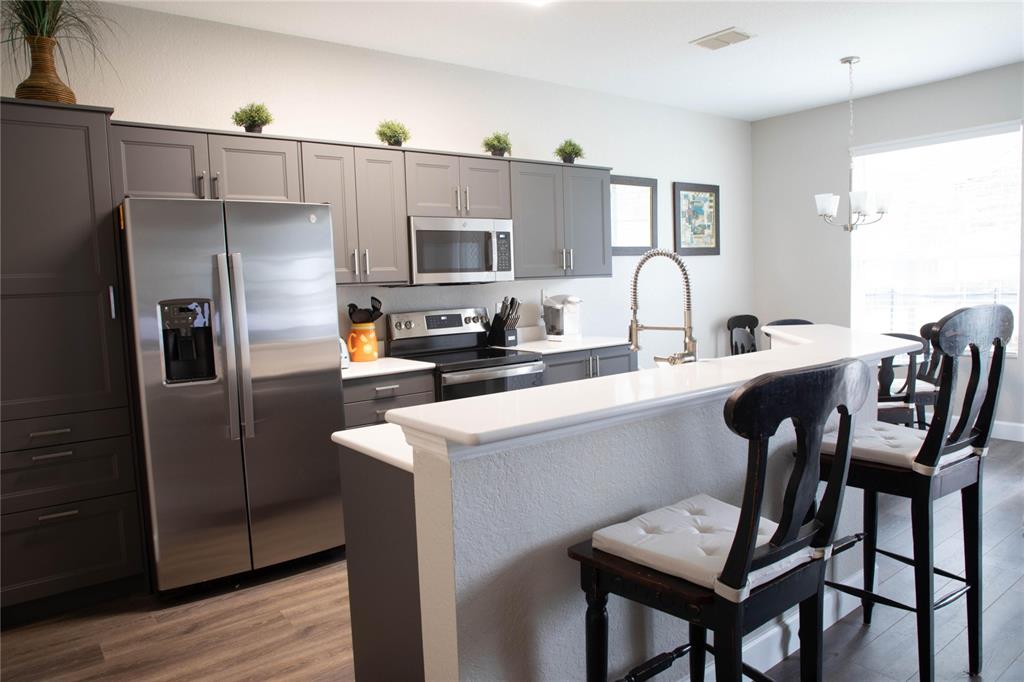 A kitchen features gray cabinets, stainless steel appliances, and a white breakfast bar with stools — 2648 DINVILLE STREET, KISSIMMEE, FL
