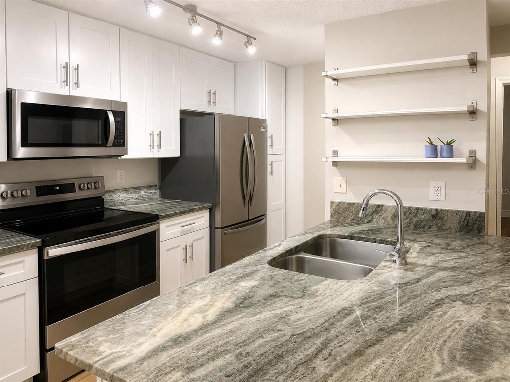 A kitchen features white cabinets, stainless steel appliances, and a green-toned granite countertop island — 956 SALT POND PLACE UNIT 204, ALTAMONTE SPRINGS, FL