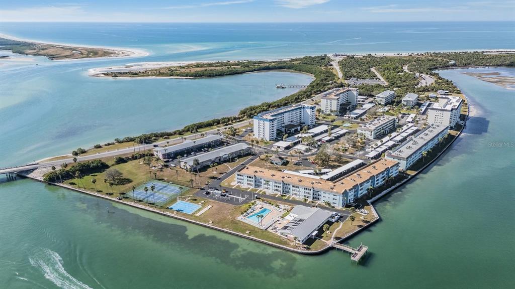 An aerial view of a coastal condominium complex surrounded by water with tennis courts — 9 HAIG PLACE UNIT 704, DUNEDIN, FL