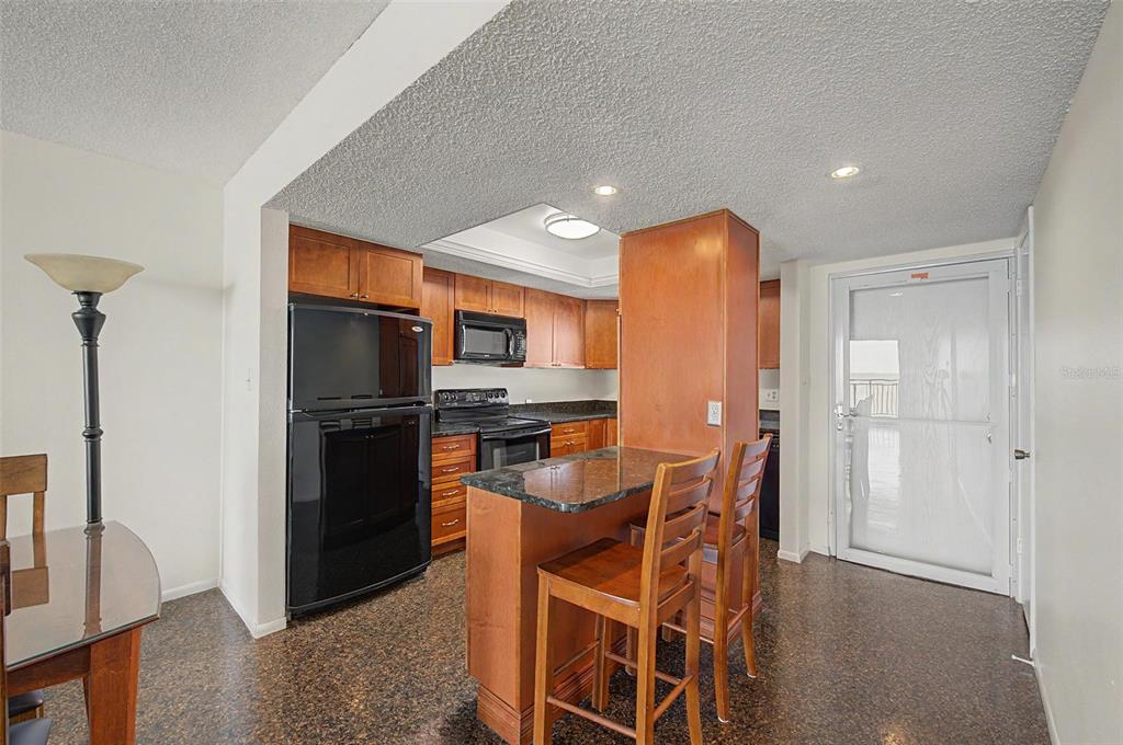 A kitchen with wood cabinets, black appliances, a granite-topped island, and dark speckled flooring — 9 HAIG PLACE UNIT 704, DUNEDIN, FL