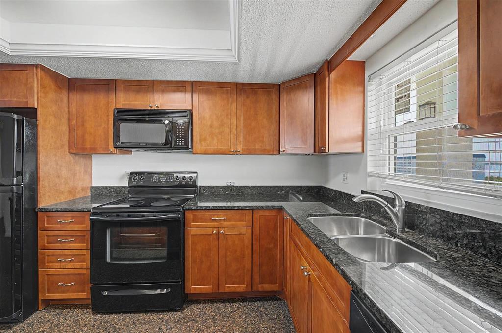 A kitchen features wood cabinets, dark granite countertops, black appliances, and a double-basin sink — 9 HAIG PLACE UNIT 704, DUNEDIN, FL