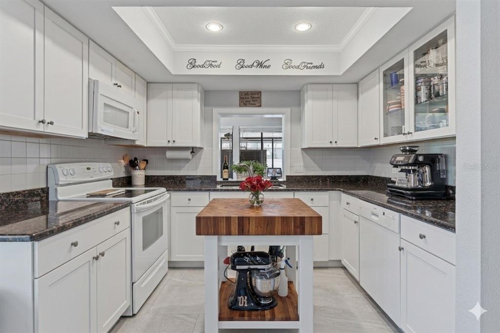 A white kitchen features a butcher block island, dark granite countertops, and a tray ceiling — 6349 PARSON BROWN DRIVE, ORLANDO, FL