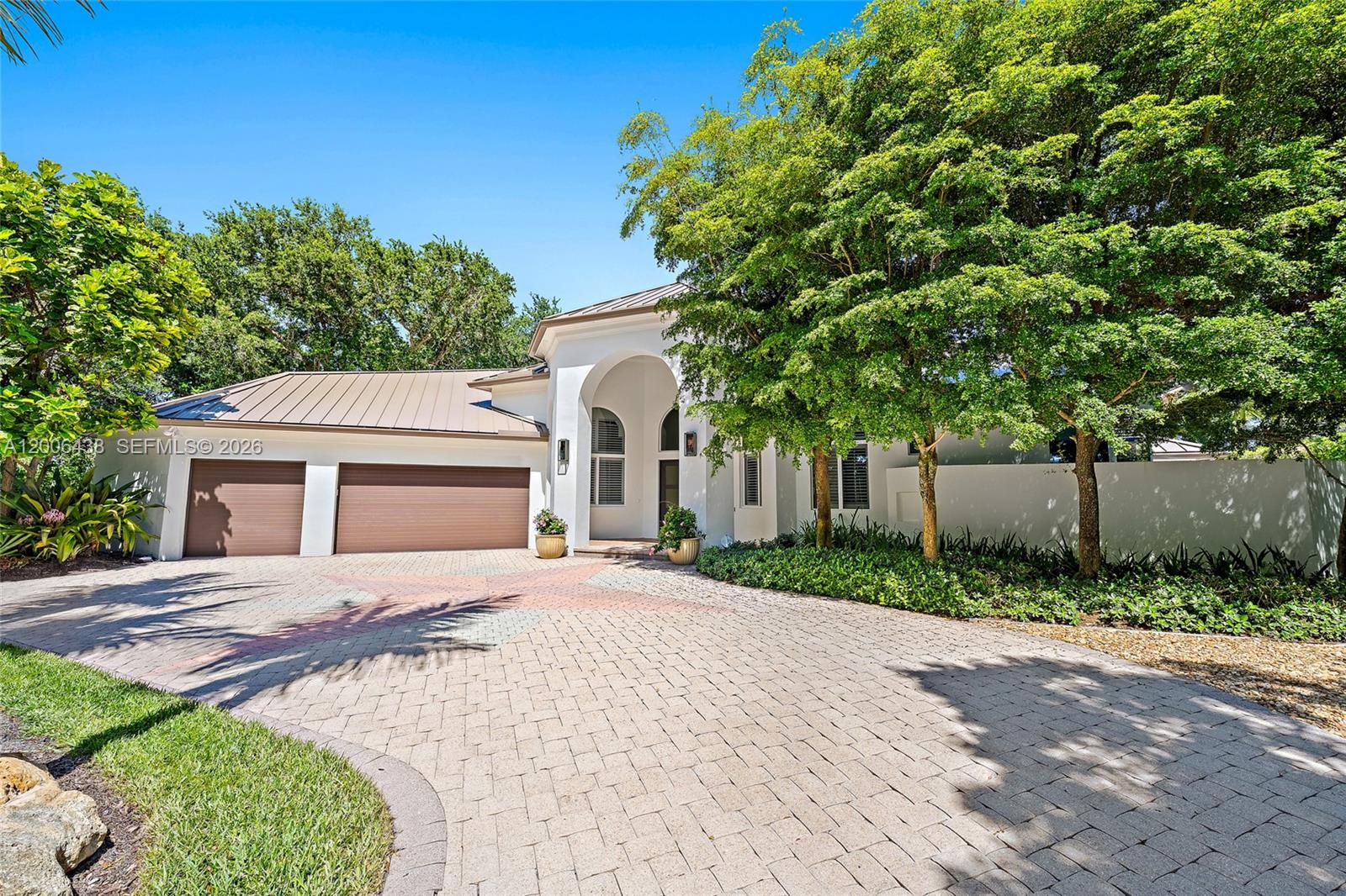The exterior of a white house features a paved driveway, two-car garage, and mature trees — 106 Commodore Dr, Jupiter FL 33477, JUPITER, FL