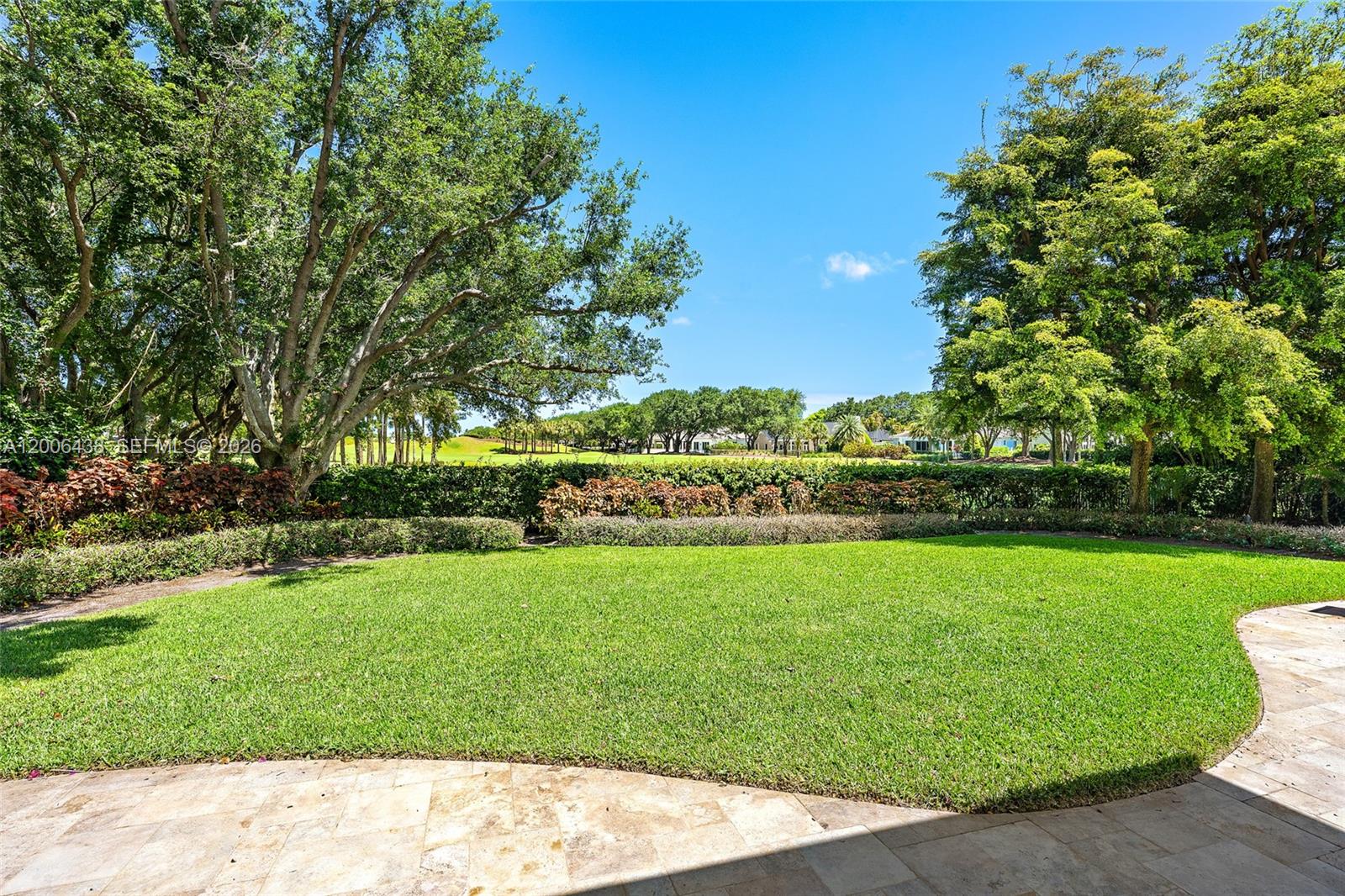 A lush green lawn extends toward a hedge and trees under a clear blue sky — 106 Commodore Dr, Jupiter FL 33477, JUPITER, FL