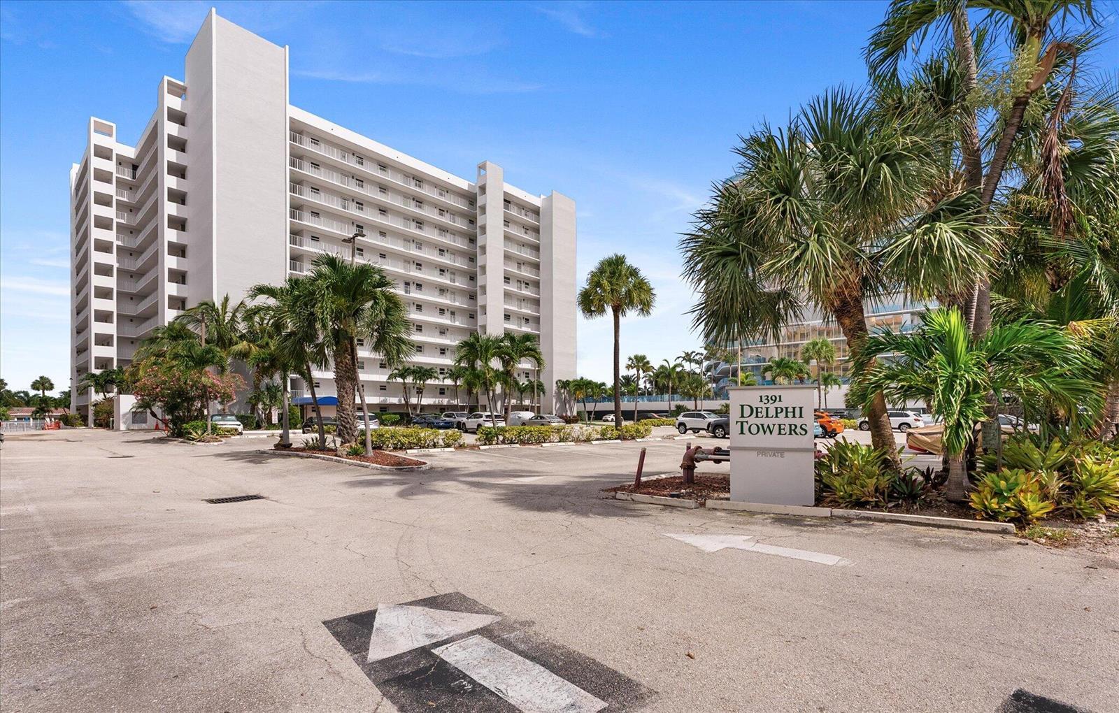An exterior view of a tall residential building with a parking lot and palm trees — 1391 S Ocean Boulevard S # 906, Pompano Beach FL 33062, POMPANO BEACH, FL