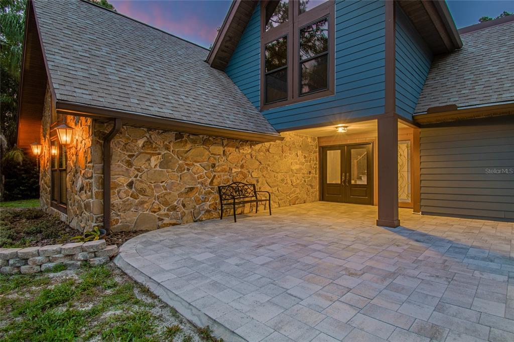 A stone-faced house exterior features a paved patio, a metal bench, and double front doors — 2120 MARQUIS COURT, NEW PORT RICHEY, FL