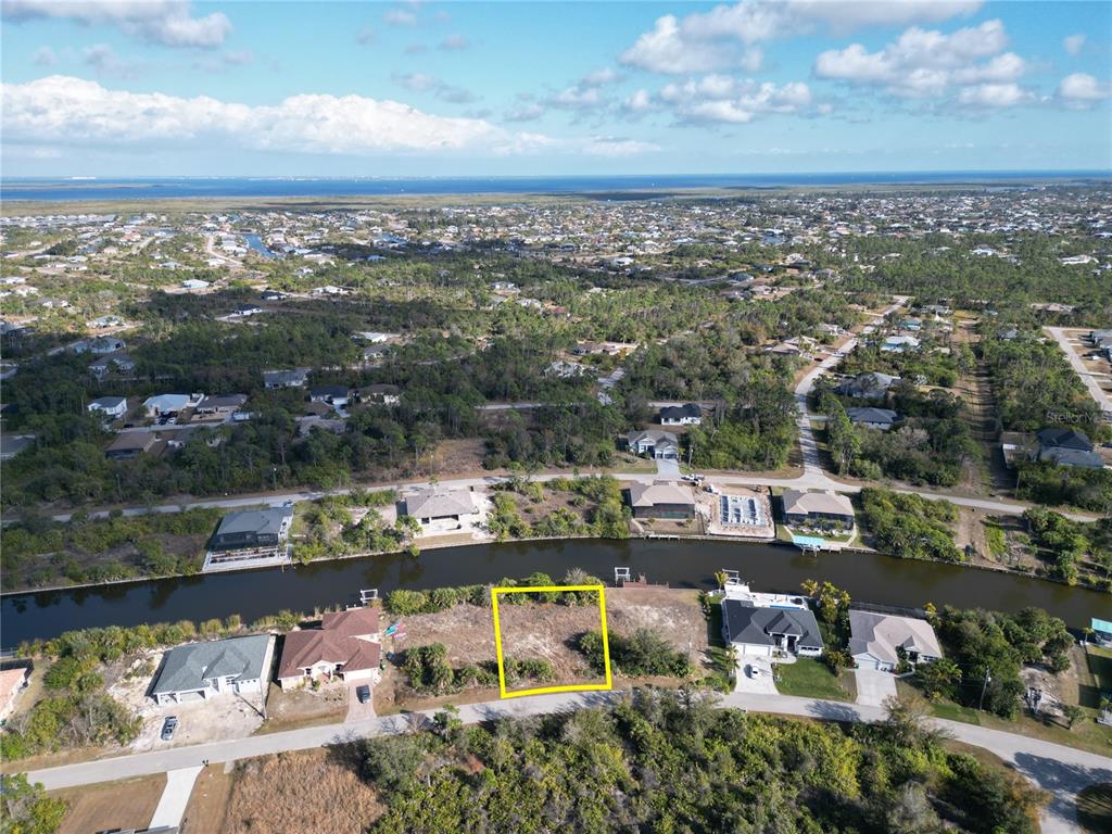 An aerial view shows a vacant waterfront lot outlined in yellow in a residential neighborhood — 8258 SANTA CRUZ DRIVE, PORT CHARLOTTE, FL
