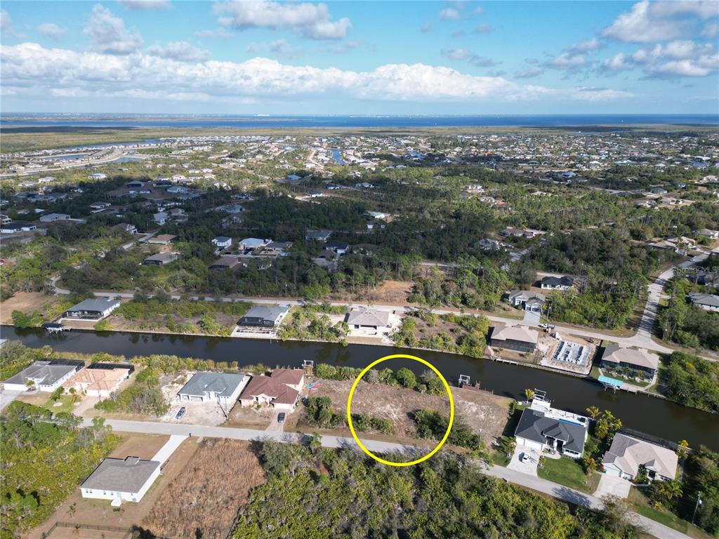 An aerial view shows a vacant, wooded waterfront lot highlighted by a yellow circle — 8258 SANTA CRUZ DRIVE, PORT CHARLOTTE, FL