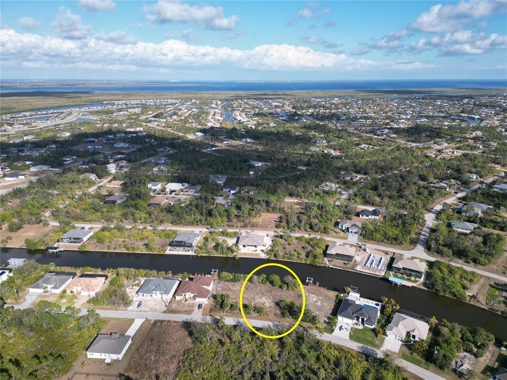 An aerial view shows a vacant waterfront lot circled in yellow within a residential neighborhood — 8258 SANTA CRUZ DRIVE, PORT CHARLOTTE, FL