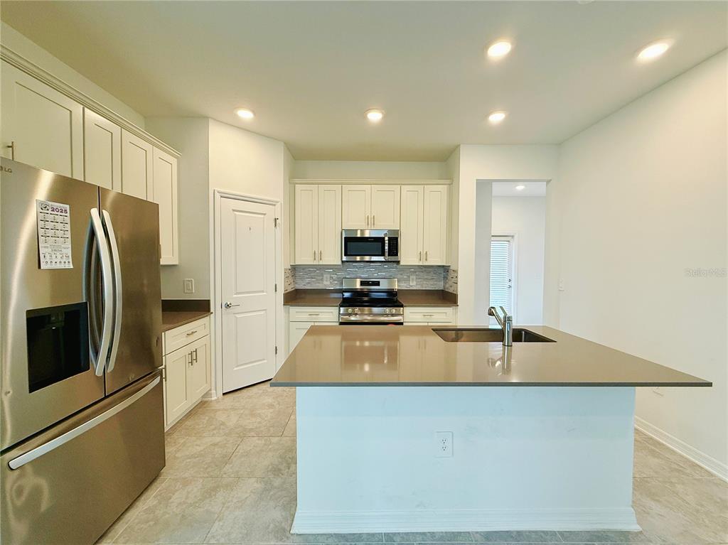 A kitchen features white cabinets, stainless steel appliances, a center island, and tile flooring — 4149 PINO STREET, APOPKA, FL