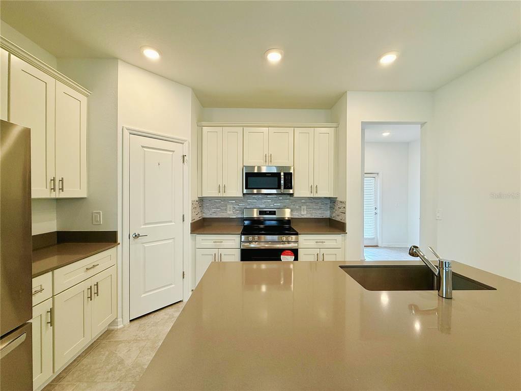 A kitchen features white cabinets, brown countertops, a central island with a sink, and stainless appliances — 4149 PINO STREET, APOPKA, FL