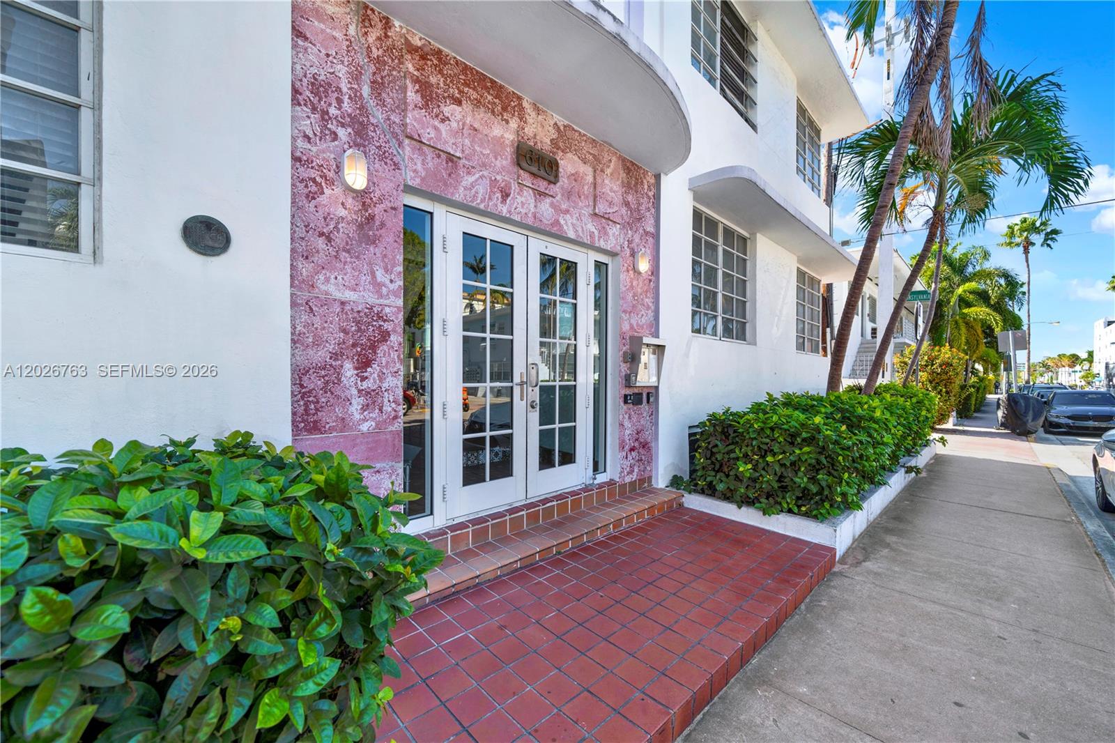 The exterior of a building features a pink stone facade, double glass doors, and landscaping — 610 8th St # 102R, Miami Beach FL 33139, MIAMI BEACH, FL