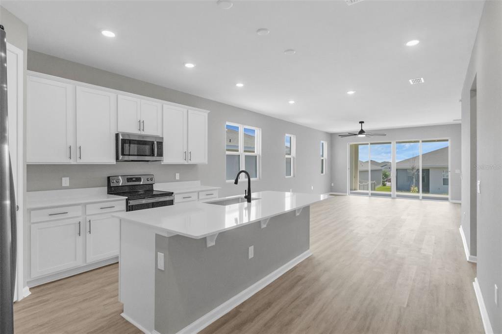 A modern kitchen with white cabinets, a quartz island, and light wood-look flooring — 819 BALLANTYNE DRIVE, LAKE WALES, FL