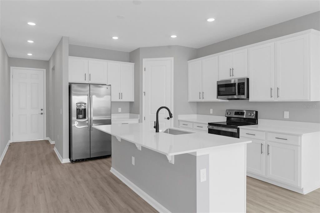 A modern kitchen features white cabinets, stainless steel appliances, a quartz island, and light flooring — 819 BALLANTYNE DRIVE, LAKE WALES, FL