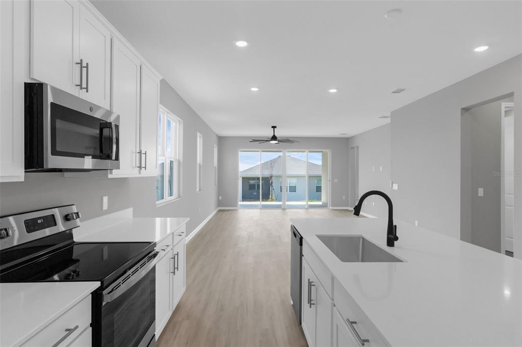 A modern kitchen with white cabinets, quartz countertops, and stainless steel appliances overlooks a living area — 819 BALLANTYNE DRIVE, LAKE WALES, FL