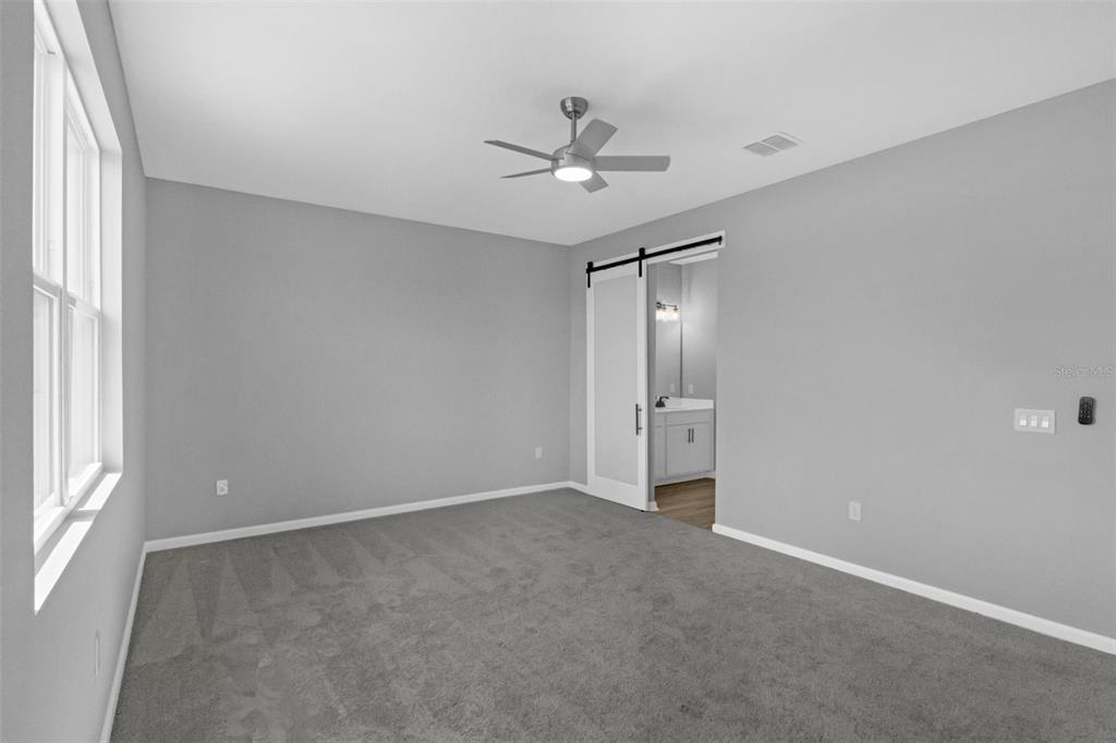 A bedroom with gray walls, gray carpeting, a ceiling fan, and a sliding barn door — 819 BALLANTYNE DRIVE, LAKE WALES, FL