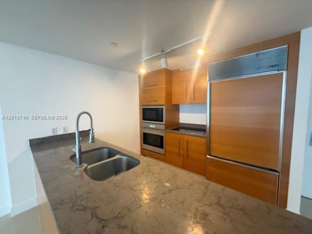 A kitchen features wood cabinetry, a stainless steel refrigerator, and a stone-topped island sink — 475 Brickell Ave # 2411, Miami FL 33131, MIAMI, FL