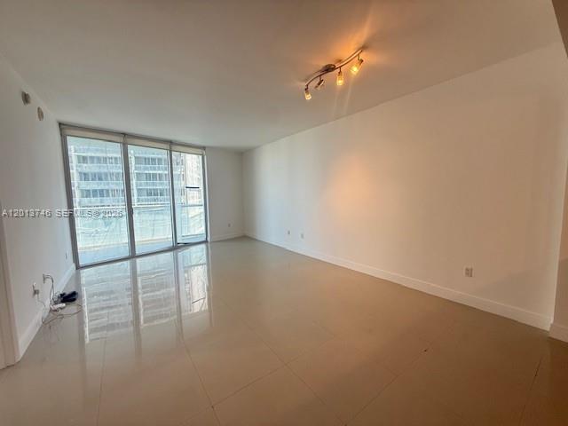 An empty living room features light tile flooring, white walls, and a glass balcony door — 475 Brickell Ave # 2411, Miami FL 33131, MIAMI, FL