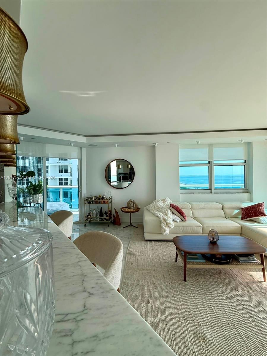 A bright living room features a white sectional sofa, marble flooring, and ocean views — 9201 Collins Ave # 826, Surfside FL 33154, SURFSIDE, FL