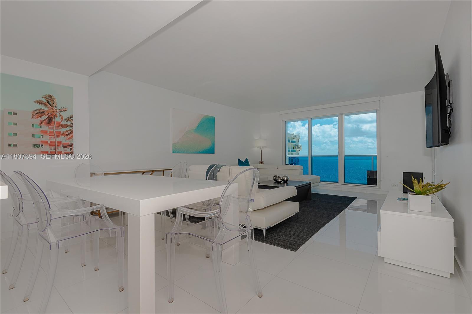 A bright living and dining area features white tile floors, clear chairs, and ocean views — 2301 Collins Ave # 1538, Miami Beach FL 33139, MIAMI BEACH, FL
