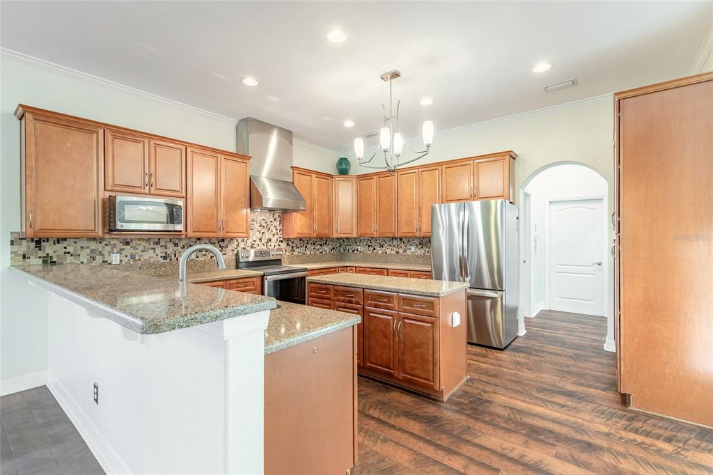 A kitchen with wood cabinets, granite countertops, stainless steel appliances, and a central island — 20 PROMENADE AT LIONSPAW, DAYTONA BEACH, FL