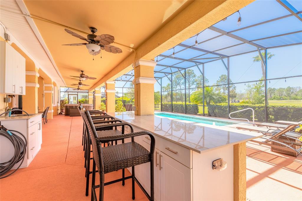 A covered outdoor kitchen and bar area overlooks a screened-in swimming pool and backyard — 20 PROMENADE AT LIONSPAW, DAYTONA BEACH, FL