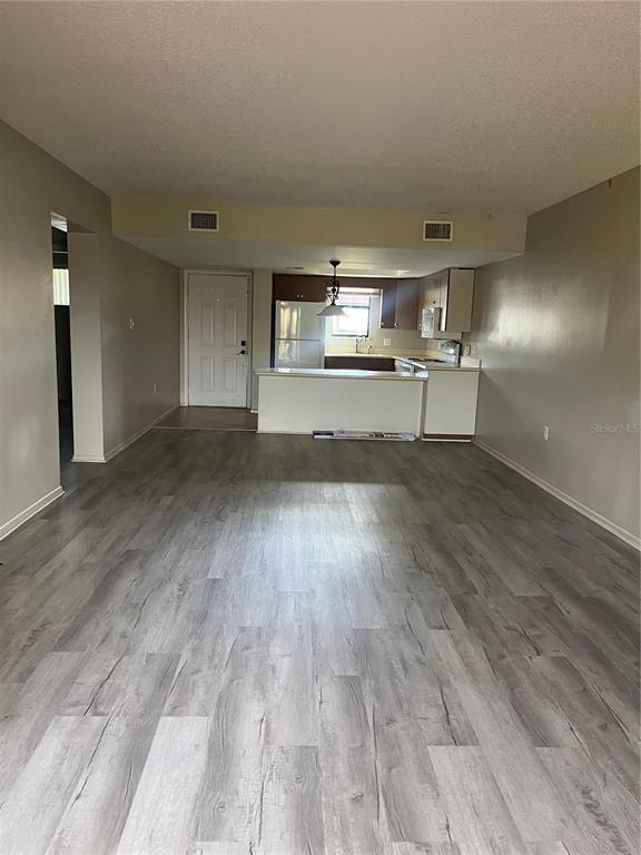 An open-concept living area features light gray wood-look flooring and a kitchen with white cabinetry — 4300 BAYWOOD BOULEVARD UNIT B105, MOUNT DORA, FL