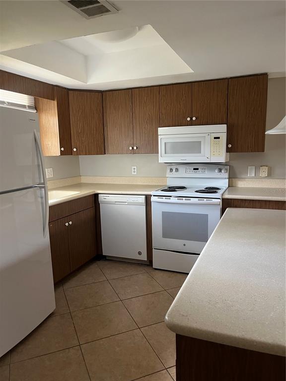 A kitchen features wood cabinets, white appliances, a light-colored countertop, and tiled flooring — 4300 BAYWOOD BOULEVARD UNIT B105, MOUNT DORA, FL