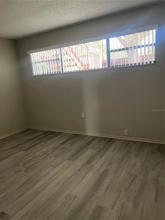 An empty room with light wood-look flooring, gray walls, and a horizontal window with blinds — 4300 BAYWOOD BOULEVARD UNIT B105, MOUNT DORA, FL
