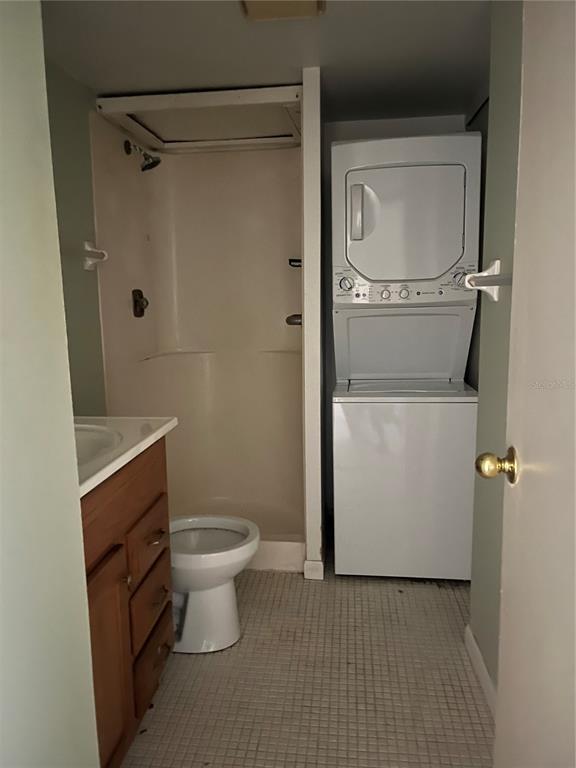 A bathroom features a vanity, toilet, shower stall, and a stacked washer and dryer unit — 4300 BAYWOOD BOULEVARD UNIT B105, MOUNT DORA, FL