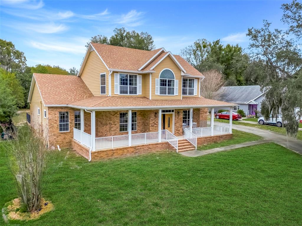 A two-story house with yellow siding, a brick lower level, and a wrap-around porch — 10336 LAKE LOUISA ROAD, CLERMONT, FL