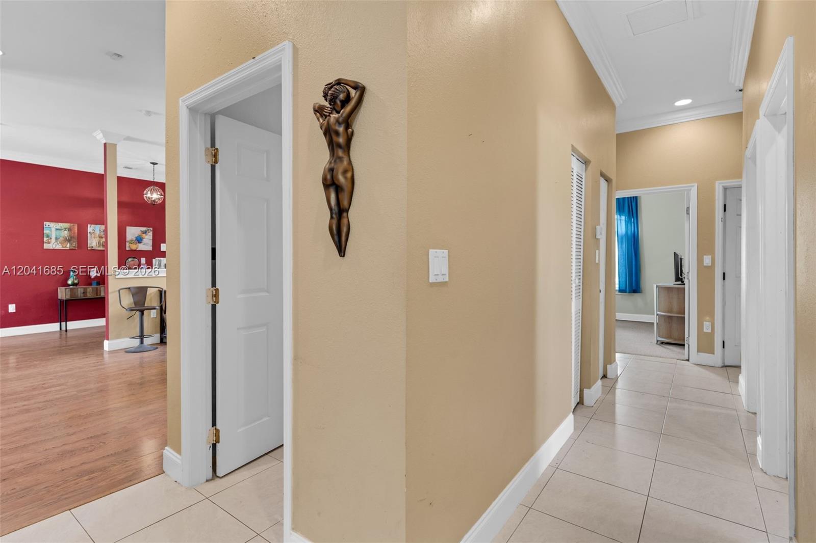 A hallway with beige walls, tile flooring, and a wall-mounted bronze sculpture leads to rooms — 7950 SW 196th Ter, Cutler Bay FL 33189, CUTLER BAY, FL