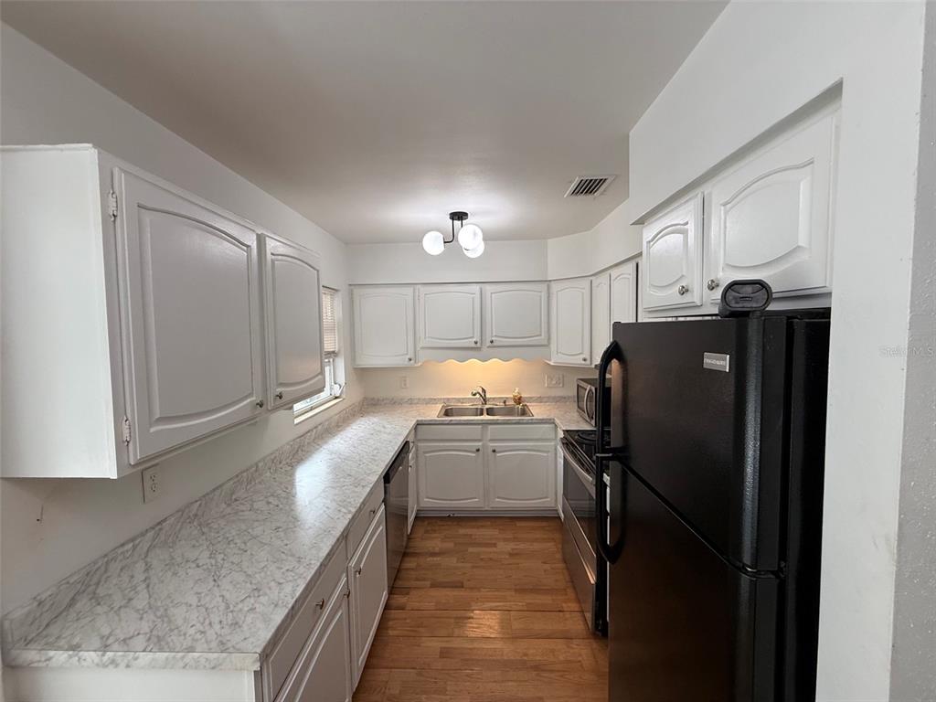 A galley kitchen features white cabinets, marble-look countertops, black appliances, and wood-style flooring — 3929 SW 21ST STREET, GAINESVILLE, FL