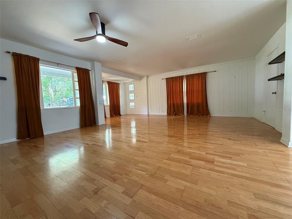 A spacious room features light wood flooring, white paneled walls, and orange curtains — 3929 SW 21ST STREET, GAINESVILLE, FL