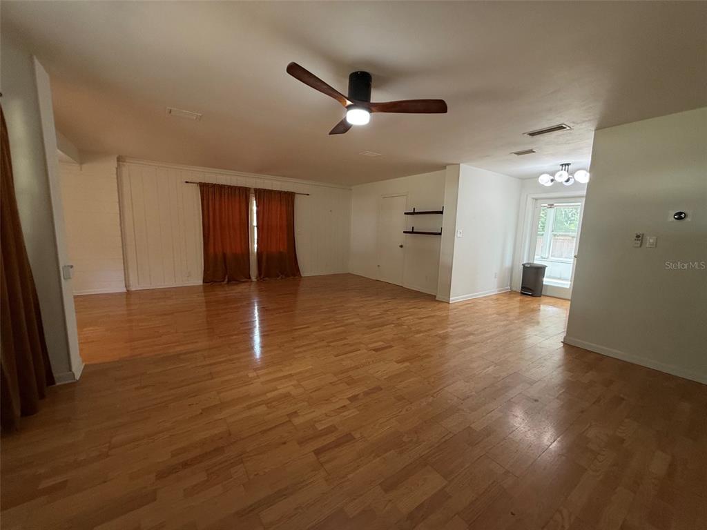 An open-concept living area features hardwood floors, a ceiling fan, and orange window curtains — 3929 SW 21ST STREET, GAINESVILLE, FL