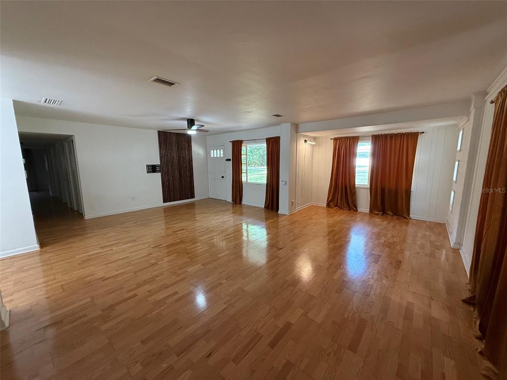 A spacious living room features hardwood floors, white walls, and large windows with orange curtains — 3929 SW 21ST STREET, GAINESVILLE, FL