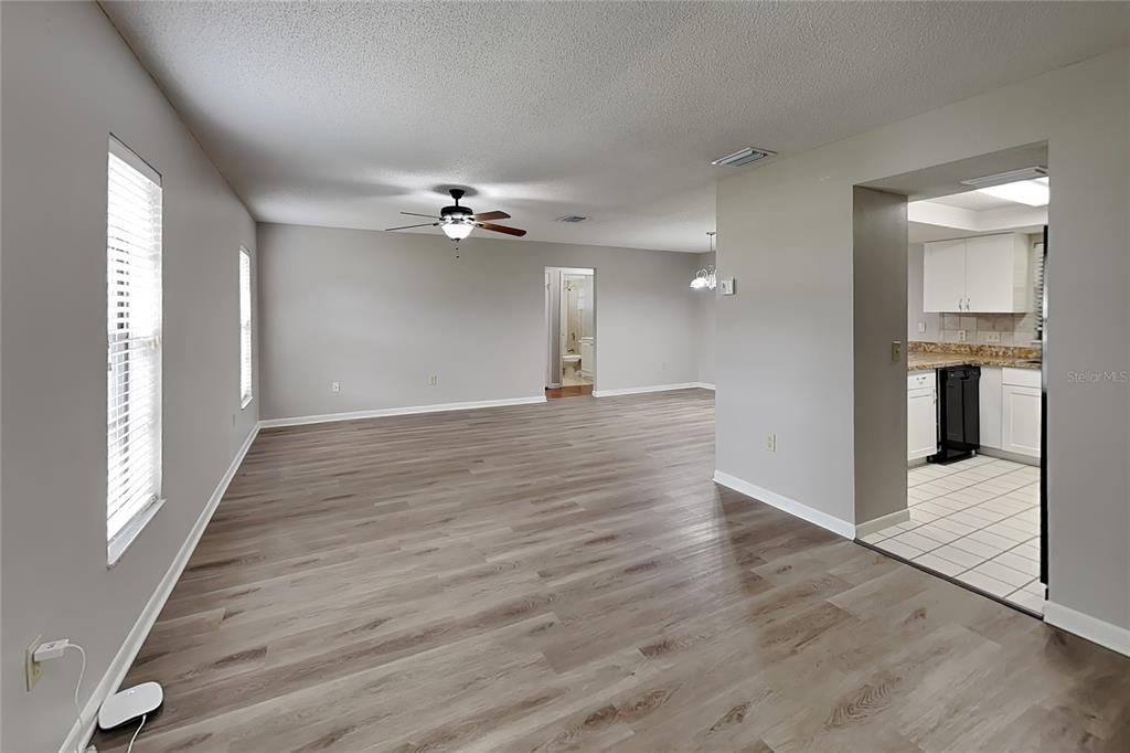 An open-concept living area features light gray walls, wood-look flooring, and an adjacent kitchen — 12207 BLUEFIELD STREET, SPRING HILL, FL