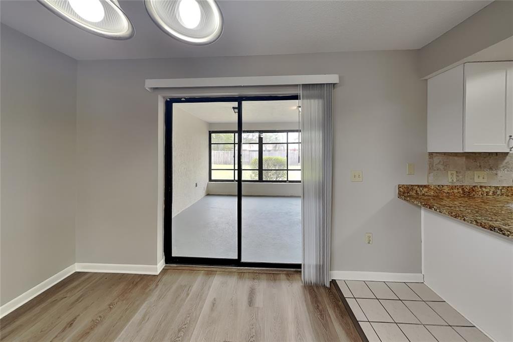 A dining area with wood-look flooring leads through a sliding glass door to a sunroom — 12207 BLUEFIELD STREET, SPRING HILL, FL