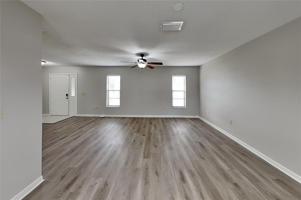 A spacious living room features light gray walls, wood-look flooring, and a ceiling fan — 12207 BLUEFIELD STREET, SPRING HILL, FL