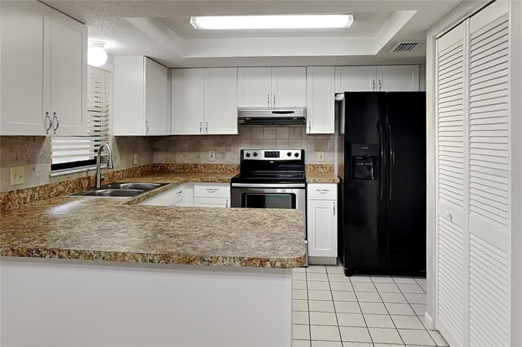 A kitchen features white cabinets, granite countertops, a black refrigerator, and a stainless steel stove — 12207 BLUEFIELD STREET, SPRING HILL, FL