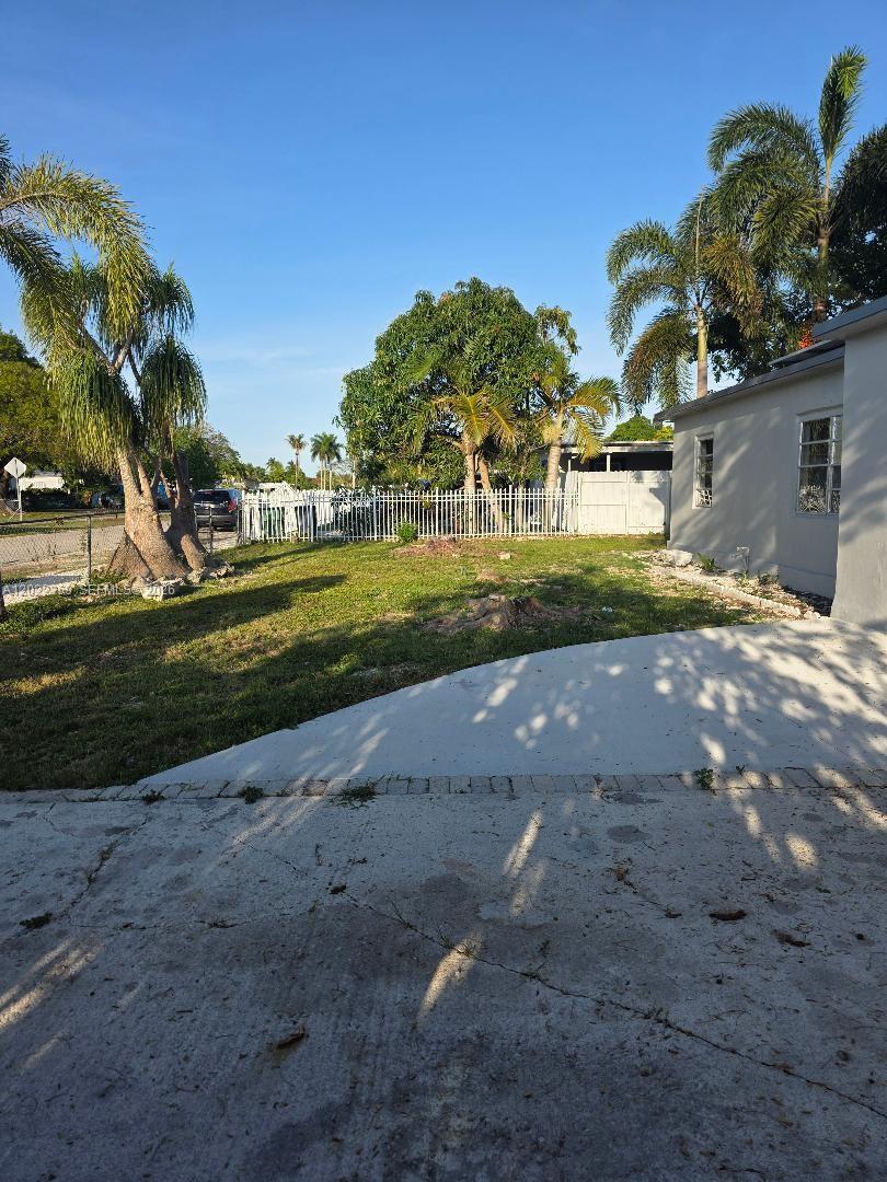 A grassy backyard features a concrete patio, palm trees, and a white metal fence — HOMESTEAD, FL