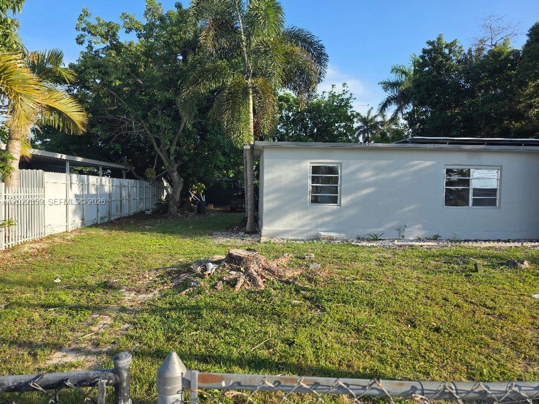 A side view of a single-story house with a yard and a tree stump — HOMESTEAD, FL