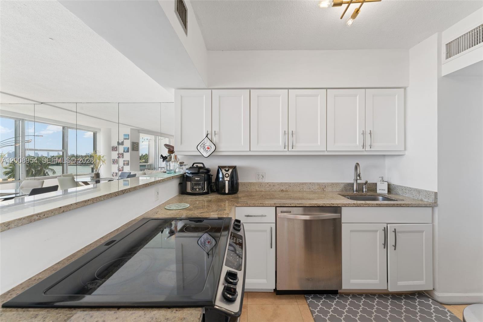 A kitchen features white cabinets, granite countertops, stainless steel appliances, and a mirrored wall — 900 Bay Dr # 421, Miami Beach FL 33141, MIAMI BEACH, FL