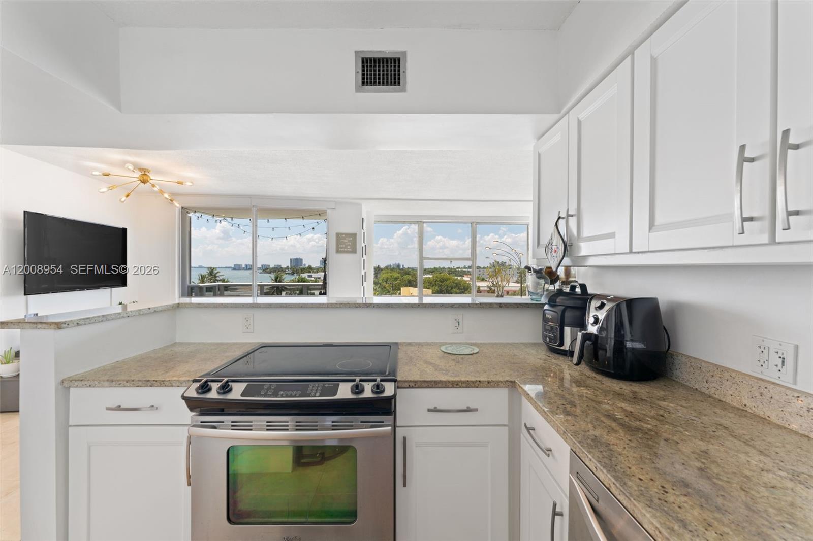 A kitchen with white cabinets, granite countertops, and a stainless steel stove overlooks a balcony — 900 Bay Dr # 421, Miami Beach FL 33141, MIAMI BEACH, FL
